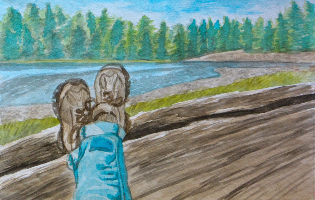 Closeup of feet wearing hiking shoes resting on large driftwood log, with bay and trees in background